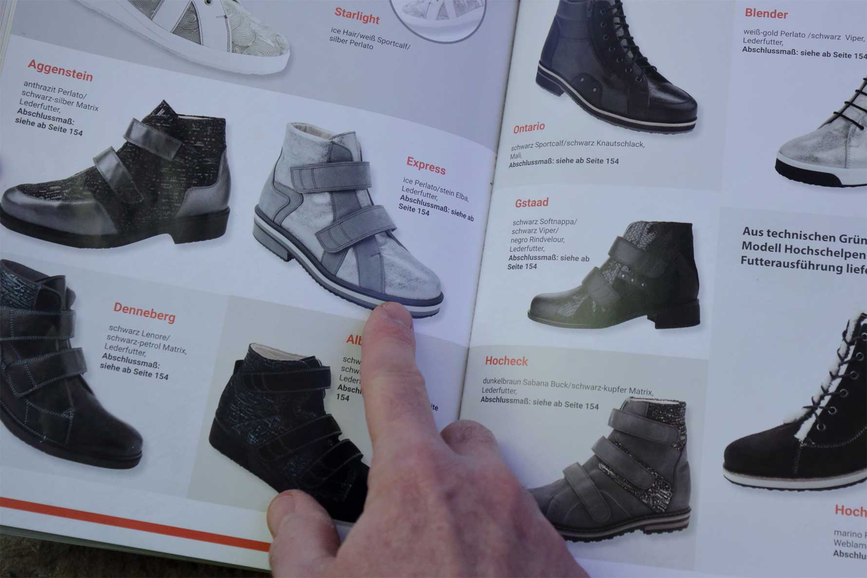 Hand zeigt auf eine Seite eines Schuhkatalogs mit verschiedenen Stiefeln und Schuhen in unterschiedlichen Designs und Farben