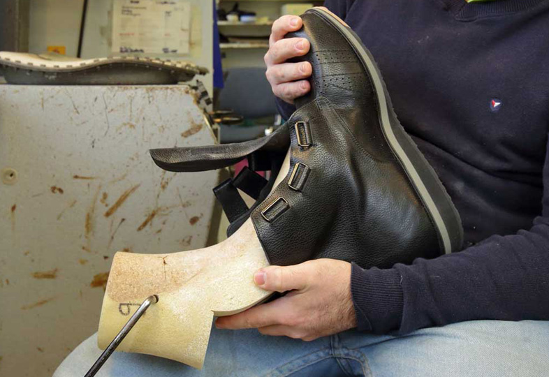 Person hält einen schwarzen Maßschuh mit drei Schnallen über eine hellbeige Schuhform aus Kunststoff