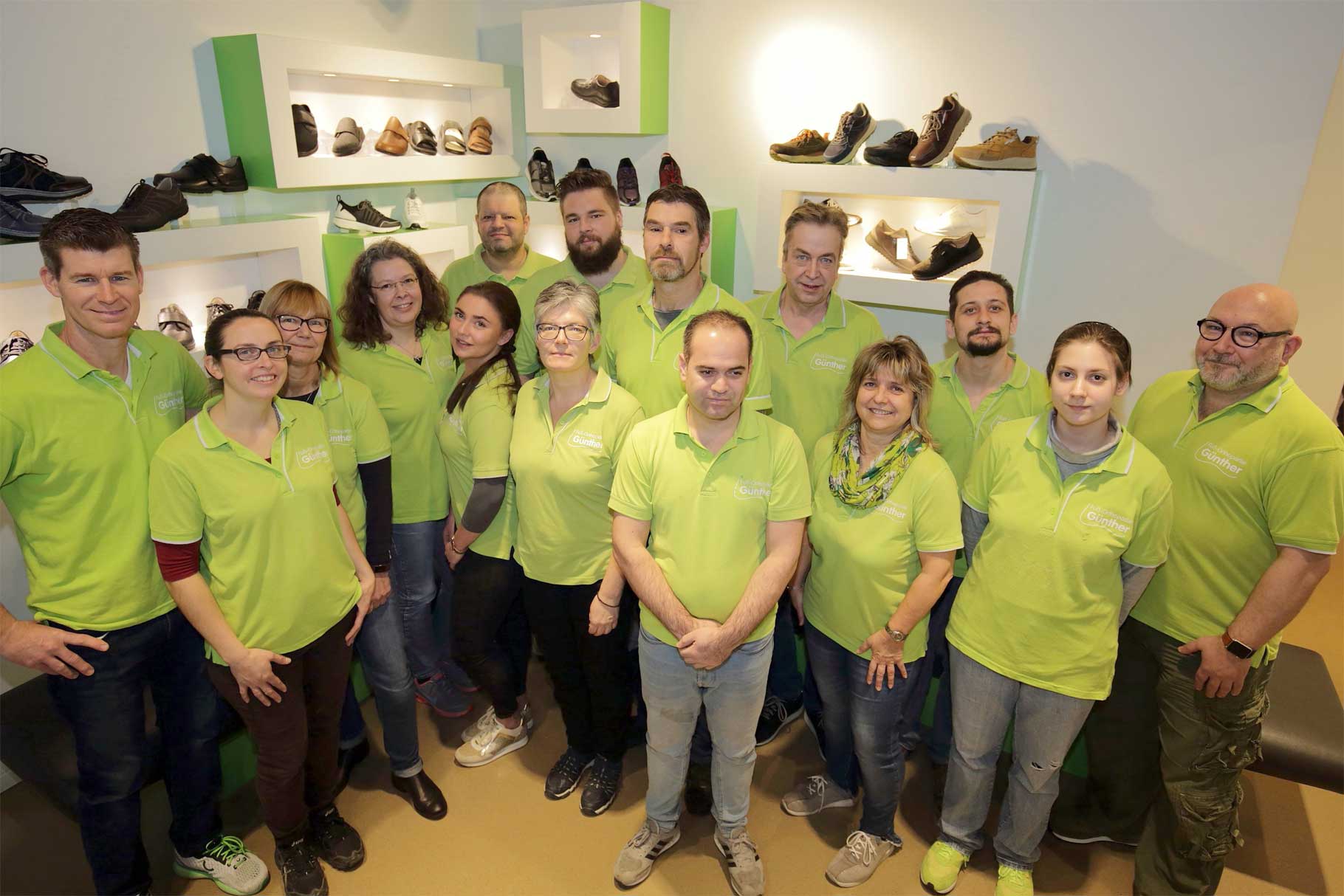 Gruppe von Menschen in grünen Poloshirts steht in einem Raum mit Schuhregalen an der Wand