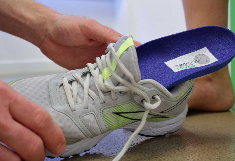 Hand setzt eine weiße Sportschuh mit grauen und gelben Details mit herausnehmbarem blauen orthopädischen Einlegesohlen ein